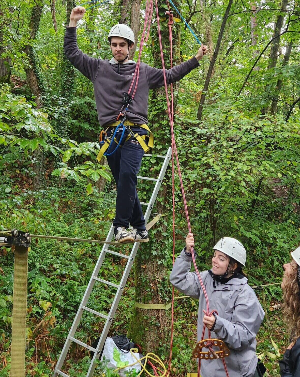 Une personne traverse une slackline installée en hauteur entre deux arbres.
