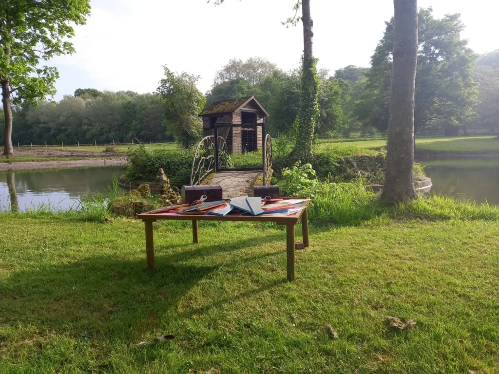 Table d'escape game en plein air avec coffres et puzzles géants au bord d'un étang en pleine nature