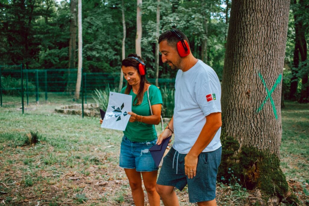 Deux participants portant des casques anti-bruit résolvent ensemble une énigme en pleine nature lors d'un escape game en forêt